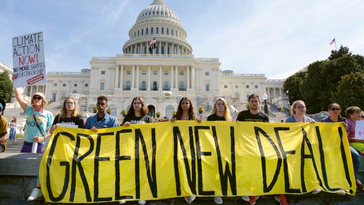 Vor den Stufen des Kapitols in Washington, D.C halten Demonstranten ein gelbes Banner mit der Aufschrift Green New Deal.