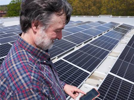 Ein Mann mit kariertem Hemd und grauem Haar steht zwischen PV-Modulen und schaut freudig auf sein Smartphone.