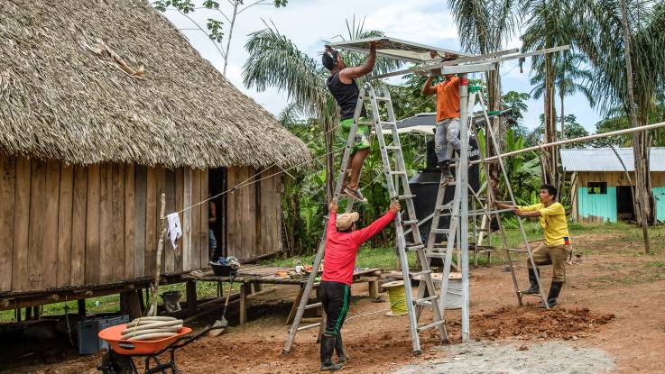 In einem Dorf mit Pfahlbauten wird ein PV-Modul mittels Leitern auf das vorgesehene Trägerwerk gehoben.