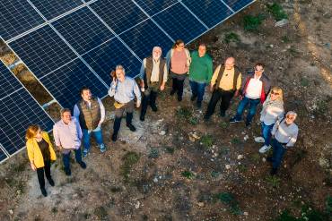 A drone photo of a group of thirteen people standing in a semicircle in front of a photovoltaic system.