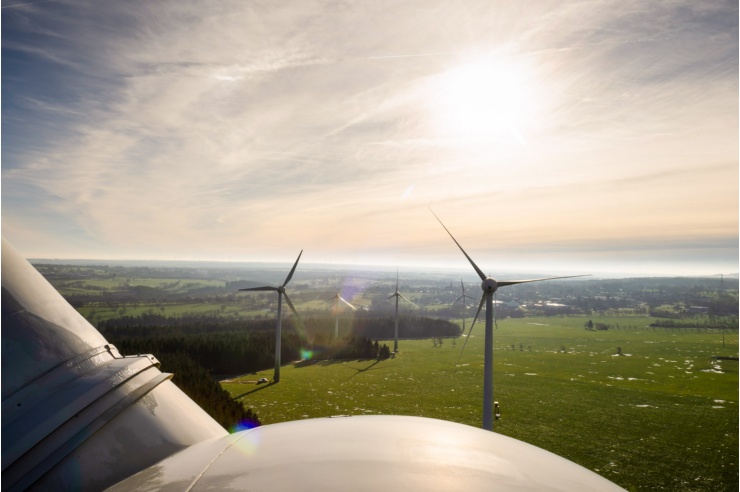 Vogelperspektive: Die Sonne steht über drei Windkraftanlagen. 