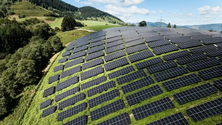 Aus der Vogelperspektive ist eine große Freiflächen PV-Anlage auf einem teils steilen Hang zu sehen. 