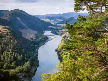 Ein Fluss schlängelt sich durch ein Tal: auf beiden Uferseiten erstreckt sich eine üppige Vegetation.