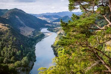 Ein Fluss schlängelt sich durch ein Tal: auf beiden Uferseiten erstreckt sich eine üppige Vegetation.