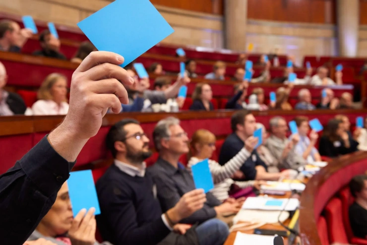 In einem klassizistischen Parlamentssaal mit rot gepolsterten Sitzen wird per Handzeichen eine Abstimmung abgehalten.