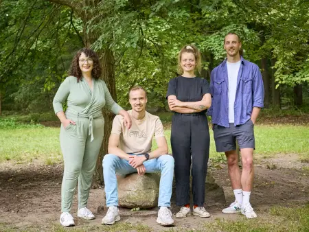 Vier Personen, zwei Männer und zwei Frauen, posieren lächelnd unter einem Baum im Freien.