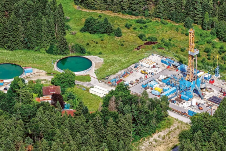 Eine Luftaufnahme zeigt einen Bohrturm und zwei große, kreisrunde Wasserbecken. Die gesamte Anlage ist von Bäumen umgeben. 