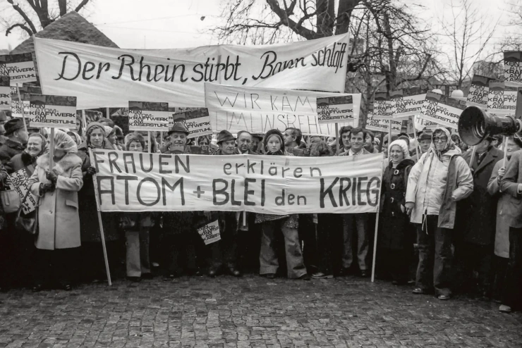 Eine Schwarz-Weiß-Aufnahme zeigt Demonstrantinnen und Demonstranten aller Altersklassen mit zahlreichen Bannern und Schildern. 